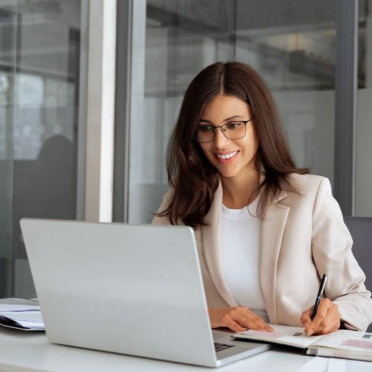 Business woman smiling at laptop while taking notes